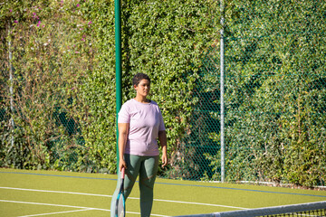 Obraz premium African american woman standing on court and holding racket in lavender shirt leggings with net