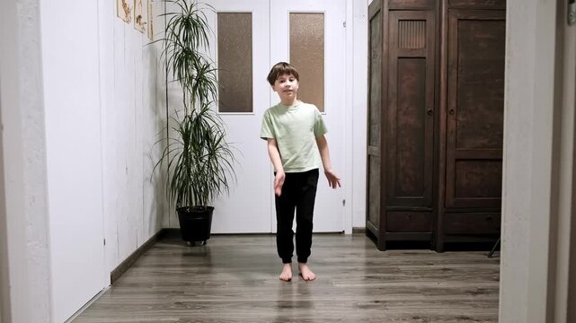 Caucasian 9 year old boy standing and alternately raises legs up with hand clap. Morning exercises of a schoolboy. Warm-up for the whole body at home. Healthy children lifestyle. Good mood. Body care.