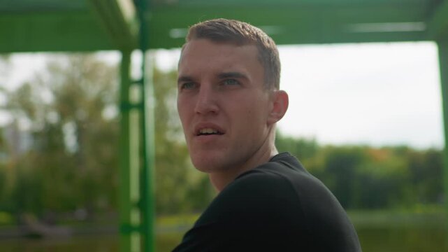 white man portrait by lake pier, closeup contemplative expressions and quiet cooldown stretch after skate session, thoughtful gaze with green structure and soft sunlight in background, mood