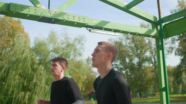two men shadowboxing under green metal pergola in park, sharp punches and controlled breathing, intense focus, speed and power training, athletic black shirts, determined expressions