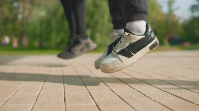 close up sneakers tapping on pavement during park rehearsal, two dancers practicing quick rhythmic footwork, worn white sneakers, textured tiles, warm sunlight, casual streetwear vibe, energetic