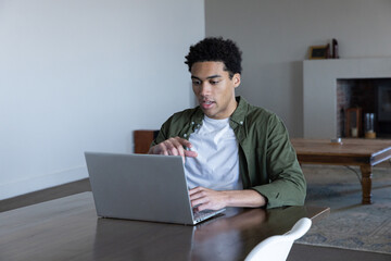 Naklejka premium African american man typing on laptop at table gesturing toward display in living room