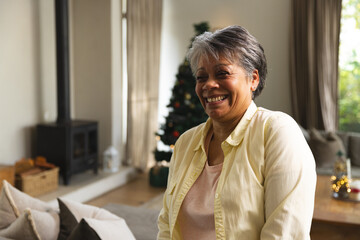 Naklejka premium Senior African American woman sitting on sofa at home near decorated Christmas tree, copy space