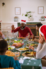 Obraz premium African american family in santa hats laughing, reaching for salad at table with tablecloth