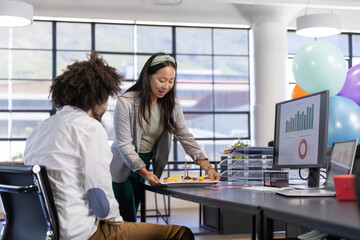 Diverse coworkers placing tray of cupcakes lit with candles on desk by window in office