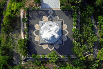 White Buddha statue sits top a hill surrounded by lush trees. Aerial top, the buildings of Nha Trang city