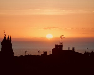 Morning sunrise with birds silhouettes on city rooftops. Beautiful dawn over the sea horizon.