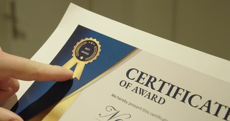 Close-up of an award certificate with a ribbon seal, touched by a finger. Concept of achievement, recognition, success, and formal appreciation.