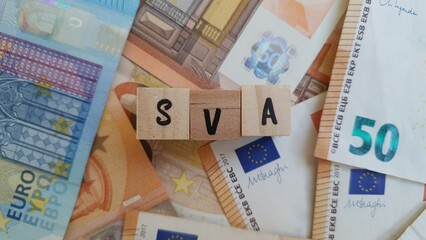 SVA acronym made of wooden letter cubes on pile of Euro banknotes. Seguro de Vida Acidente (Life Accident Insurance)