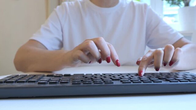 Woman is typing on a keyboard. She has red nails and is wearing a white shirt. The keyboard is black and has a white space bar