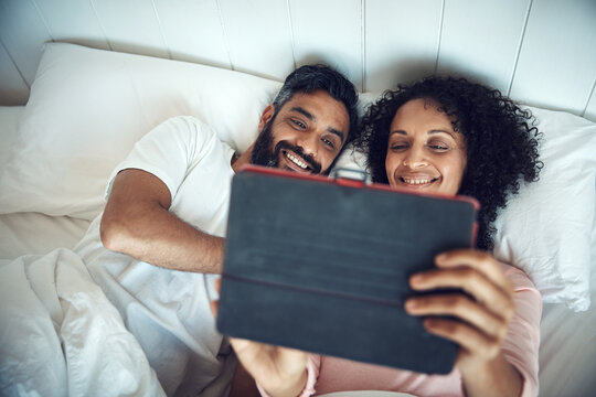 Happy, couple and relax on bed with tablet, streaming service and watching movie for bonding together. Above, married people and smile in house with digital technology, series and show on weekend. - Powered by Adobe