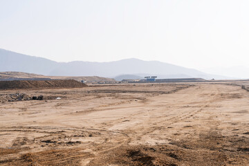 construction site with dirt road and barren land under clear sky, showing early stage infrastructure development and wide open space for future projects.