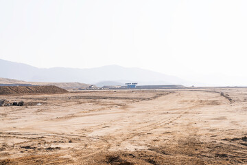 construction site with dirt road and barren land under clear sky, showing early stage infrastructure development and wide open space for future projects.