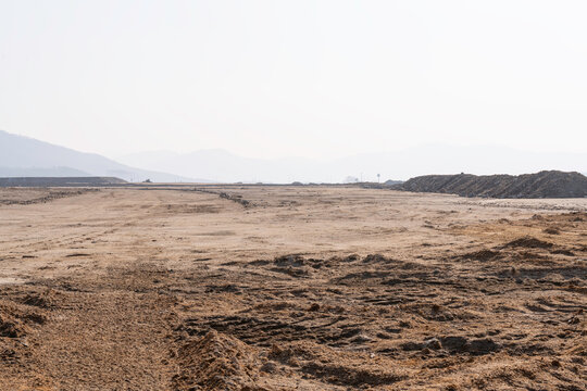 construction site with dirt road and barren land under clear sky, showing early stage infrastructure development and wide open space for future projects.