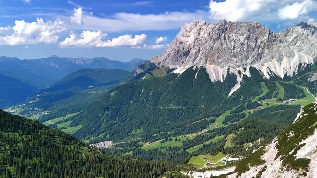 Aerial drone view of the Alps on a sunny summer day. Green alpine landscape with rolling hills, mountain peaks, blue sky and natural scenic panorama. Travel destination, nature background.