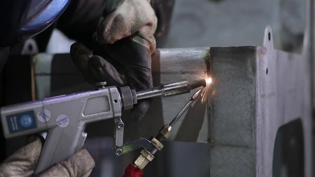 Worker performing manual laser welding on metal part
