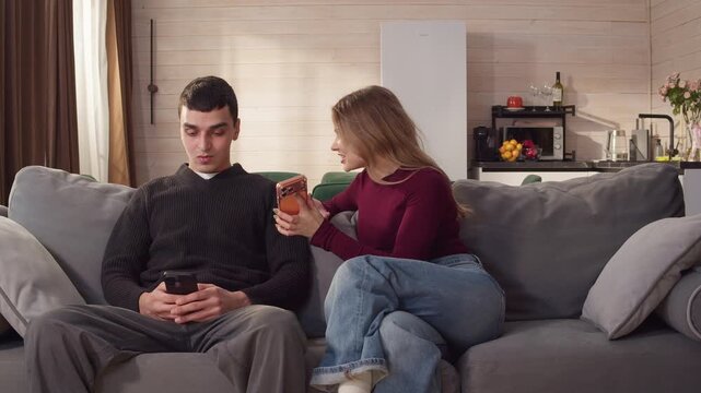 Sad ignore couple sit couch home using smartphone. Addict social media, relationship coldness issue. Cell mobile phone scroll problem. Useless cellphone internet surfing. Man have resentment, quarrel.