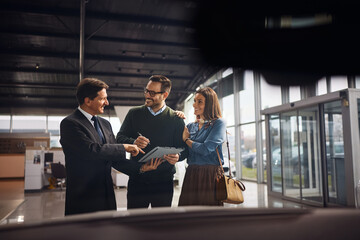 Happy couple signing a contract with a salesman at car dealership.