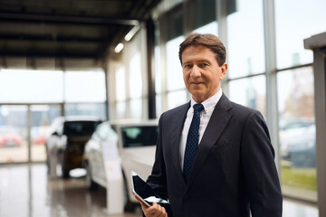Fototapeta premium Mature salesman at car dealership looking at camera.
