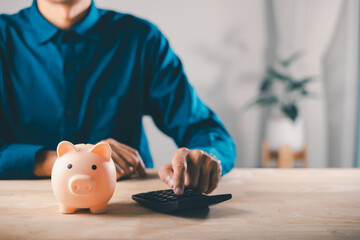 Man uses calculator and piggy bank money to save for tax plan saving, retirement, financial invest...