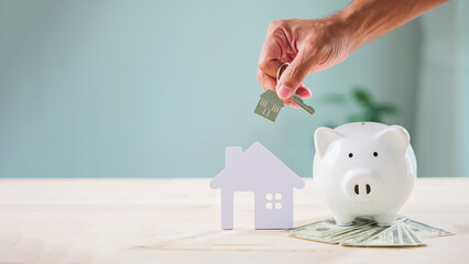 Hand offers house key above paper home model for bank piggy saving security, important for financial future, personal privacy, cyber protection