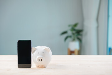 Digital savings mobile payment bank piggy phone payment online save smartphone pig app illustrates white ceramic money box beside black cellphone on light wooden table for finance growth