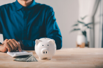 Businessman manages bank piggy savings money financial business loans saving plan, tracking financial analytics plus kpi metrics while using calculator with cash on wooden table