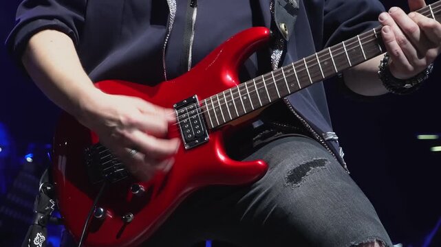 Man plays bass guitar entertaining audience at concert closeup. Talented musician in black jacket performs string instrument solo on stage
