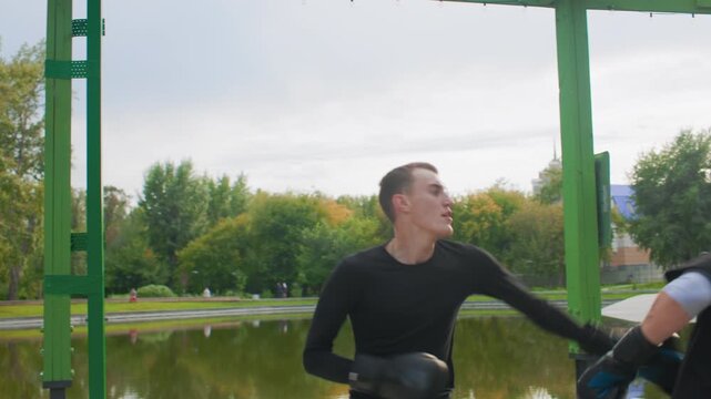 Lakeside counterattack practice two men trading powerful hooks and counters under green shelter, explosive strike, tight guard, rapid footwork, tense expressions, water reflection and park backdrop.