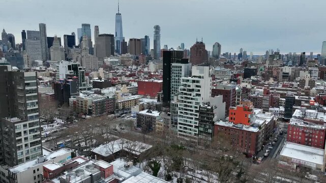 Snow-covered New York City skyline with dense urban rooftops and skyscrapers under an overcast winter sky, America metropolis during cold season. Aerial wide shot.
