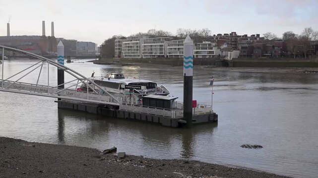 MBNA Uber Boat glides along the Thames, pulling into Vauxhall pier with the riverside skyline and government building in the background.