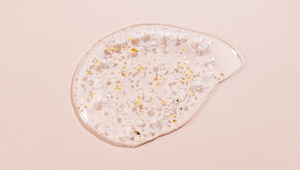 Serum fluid 24k gold gel facial cream smear, on beige pastel background. Beauty cosmetic product smudge, pure transparent lotion with gold particles, skin care jelly serum, top view luxury moisturizer