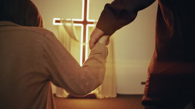 Close-up of the hands of a father and son walking towards a glowing cross in a church