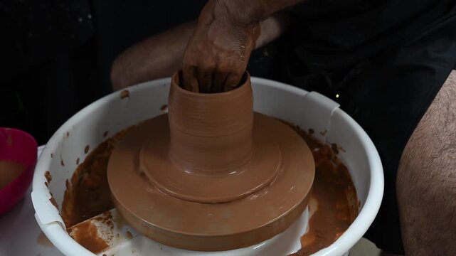 Male potter using a pottery wheel to demonstrate the basic pulling up technique to form a clay cylinder, traditional ceramic craftsmanship.