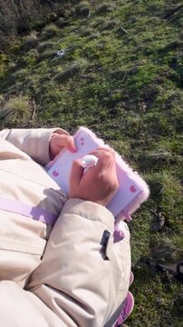 Top-Down View of Little Girl Drawing in Small Pink Notebook Outdoors, 10 Seconds

