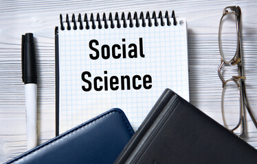 SOCIAL SCIENCE - words in white paper on the background of a diary, glasses and pen