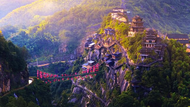 Aerial shot of traditional Chinese wooden houses built on a steep cliff in Wangxian Valley, Jiangxi, China during a golden sunset.