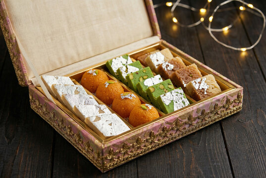 Assorted Indian sweets gift box with Kaju Katli, Ladoo, and Burfi on wooden table with festive lights