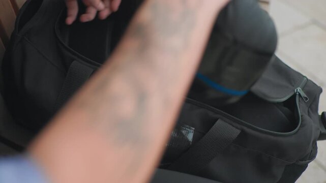 white person discovers blue pouch inside duffel, fingers trace taped seam and pull out bright organizer closeup of tattooed forearms over tiled floor, tactile surprise and careful inspection frames