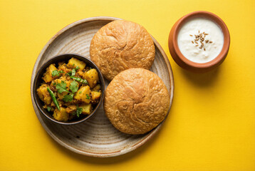 A plate of Aloo Puri featuring fried puffy bread and potato curry served with a side of fresh yogurt on a yellow background