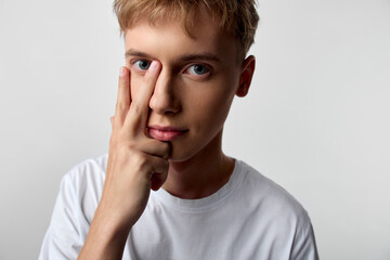 Closeup of a young man in a white shirt making a two finger gesture by the eye, conveying curiosity, focus and playful mood with clean studio lighting and plain background for fashion, lifestyle, or