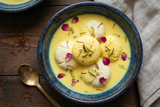 A blue bowl filled with Rasmalai, an Indian dessert of cottage cheese balls in saffron milk, garnished with rose petals