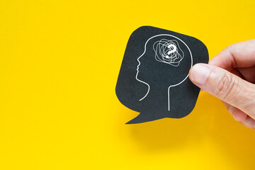 Mental health, brain disorder, World mental health day, Alzheimer, Psychology concept. Hand hold real black speech bubble paper cut with tangle of thoughts inside head on yellow background