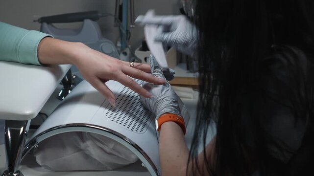 Salon technician giving desired shape to fake nail during cosmetic manicure procedure
