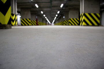Low-angle view of an empty underground parking garage with concrete floors, fluorescent lights, and...