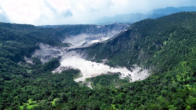 Cinematic drone shot of a Majestic Tangkuban Perahu volcanic crater in Bandung, Indonesia surrounded by lush green forest and mountains under a cloudy sky