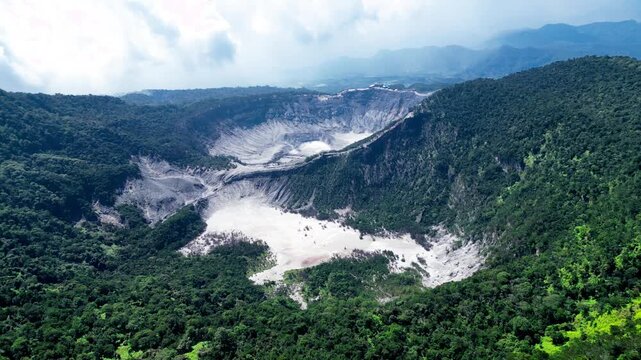 Aerial view of a Majestic Tangkuban Perahu volcanic crater in Bandung, Indonesia surrounded by lush green forest and mountains under a cloudy sky