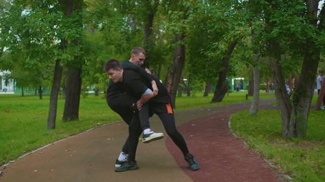 Park confrontation between white men, sparring turns into aggressive assault with takedown and pin on pathway, playground in background, hard pavement, frantic gestures, pleading and shove, tense