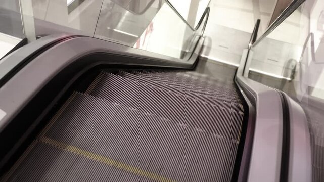 Tilted perspective of a clean, empty escalator going down in a modern indoor setting, featuring metal steps with yellow edges and glass side panels