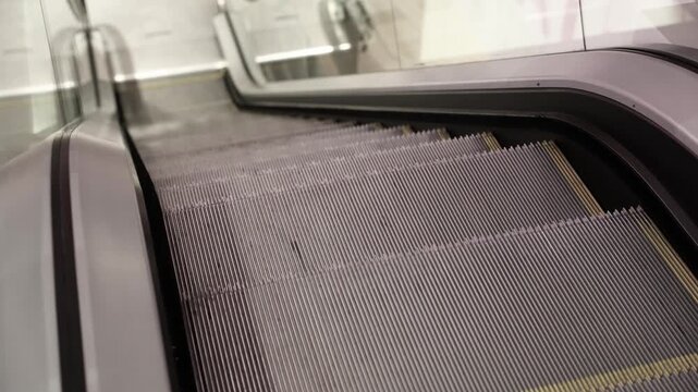 Tilted perspective of a clean, empty escalator going down in a modern indoor setting, featuring metal steps with yellow edges and glass side panels